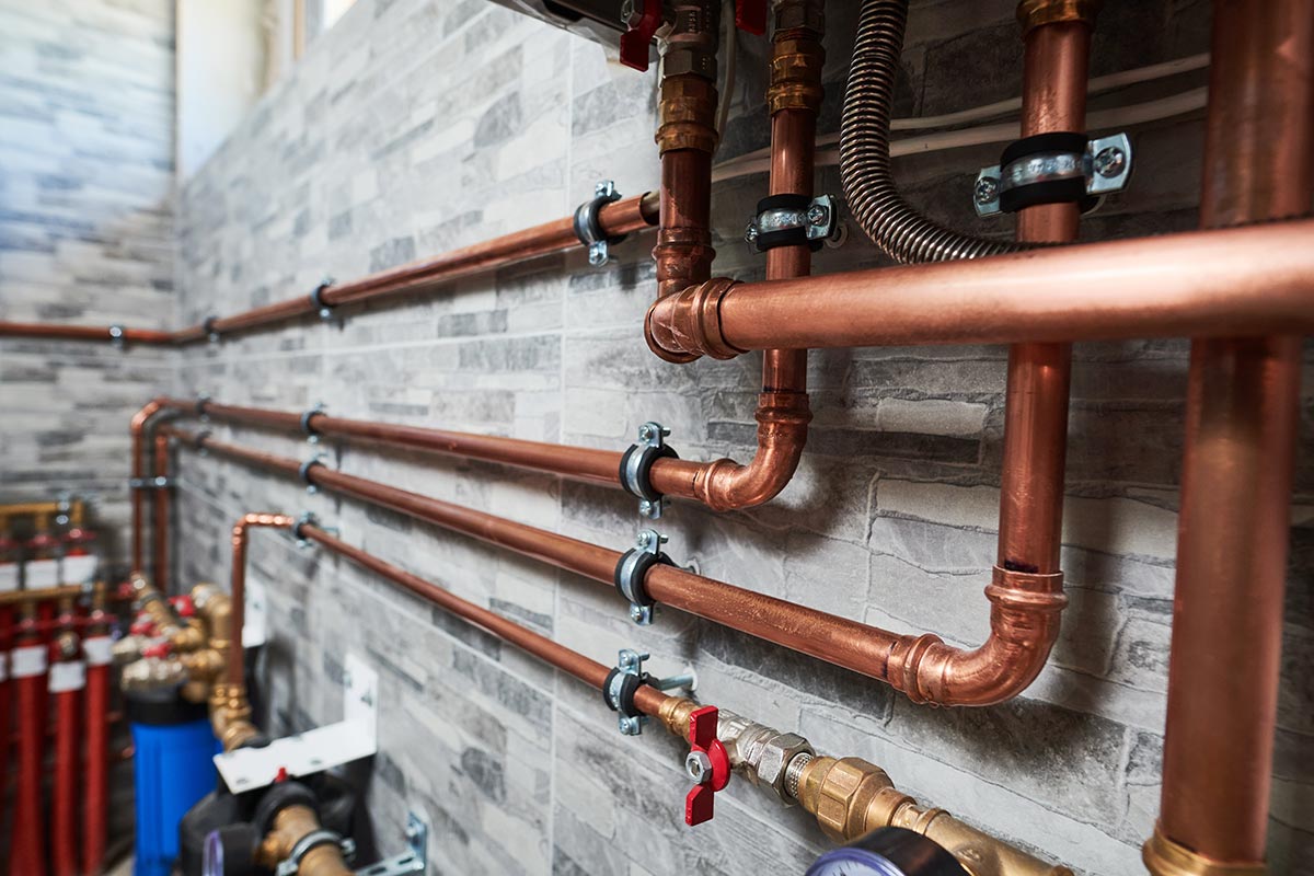 Copper plumbing pipes installed with fittings along a masonry wall