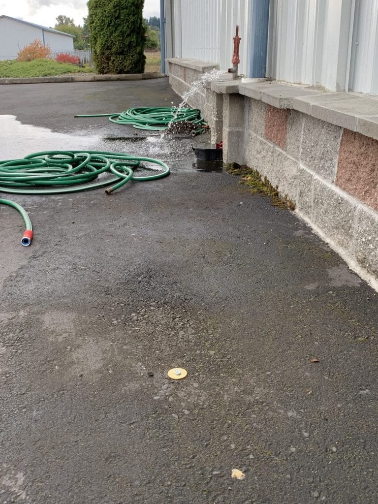 Commercial property with an underground PVC water pipe leak spraying beside the building