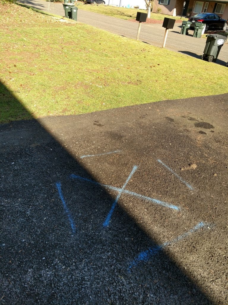 Chalk X marks on driveway indicating underground water pipe leak location