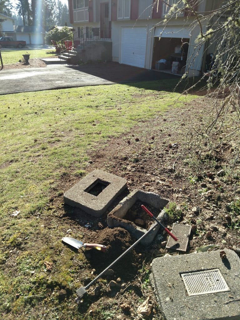 Excavated concrete meter box in front yard showing underground pipe access