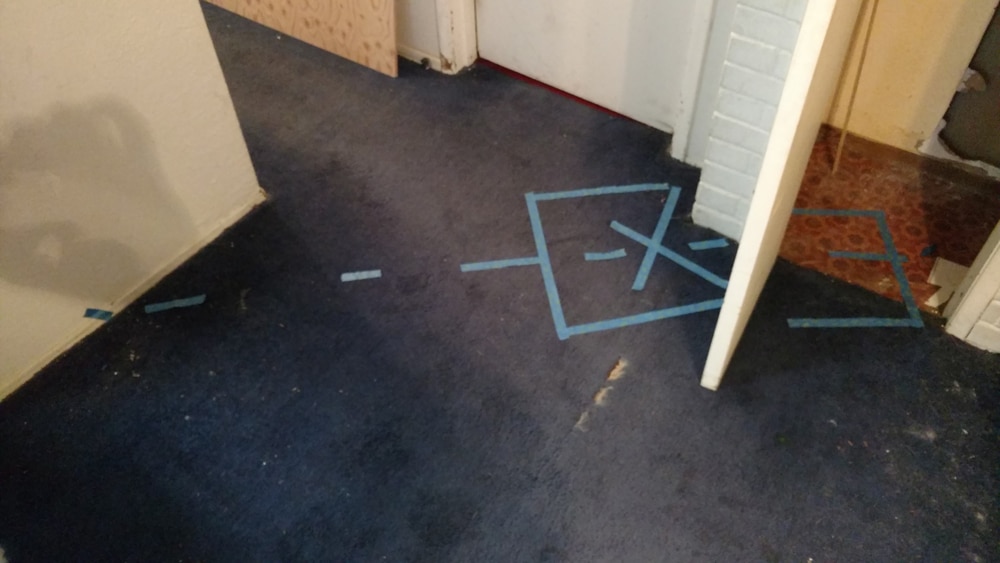 Blue tape marks the detected location of an indoor residential leak beneath the ground floor