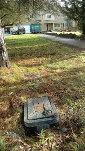 Water meter box in grass with house and driveway in background