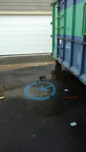 Blue spray paint circle on driveway next to dumpster pinpoints the leak
