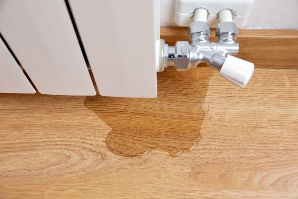 Water pooling on a hardwood floor beneath a leaking radiator pipe