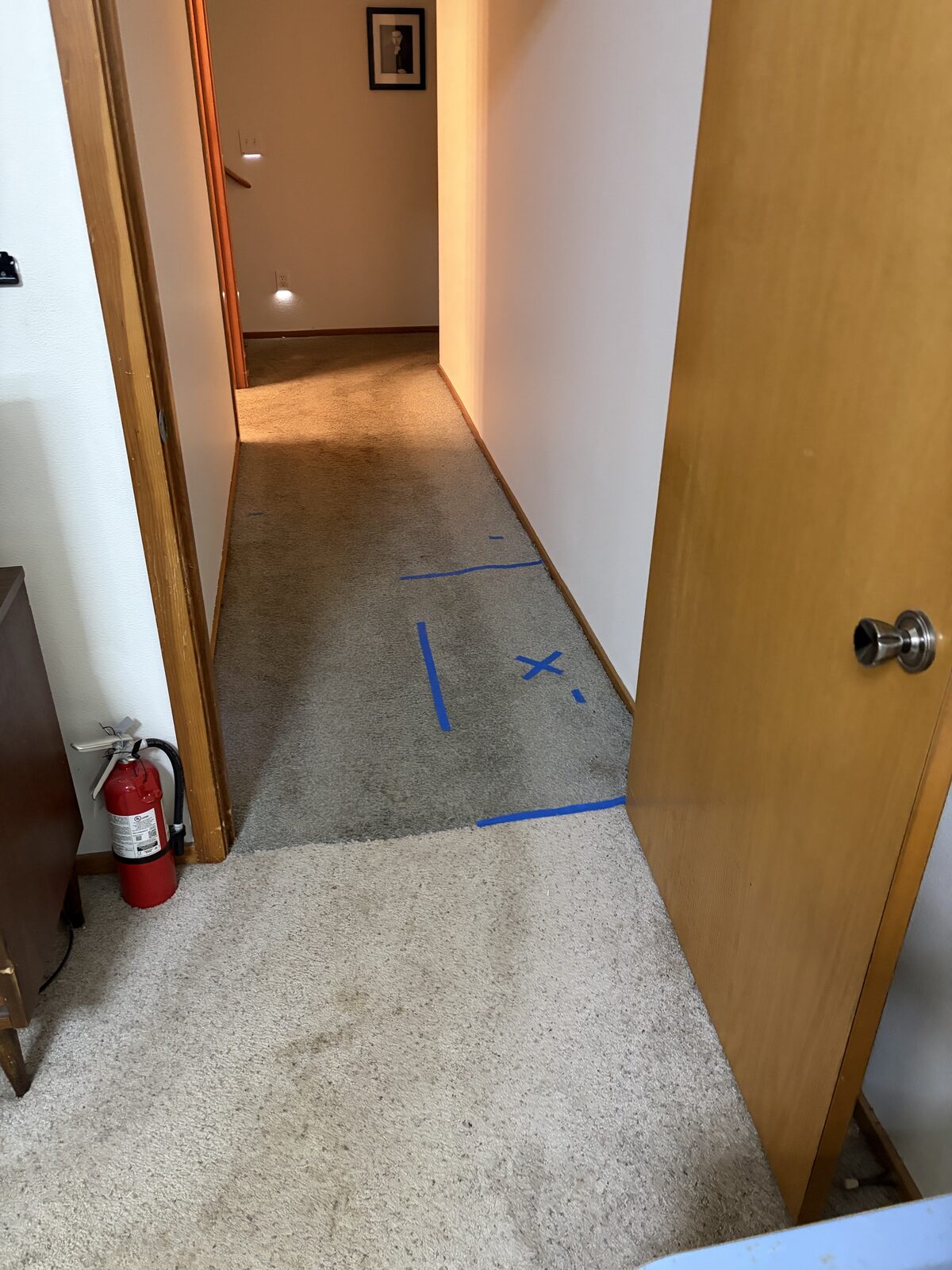 Blue tape marking a located residential leak beneath a hallway floor