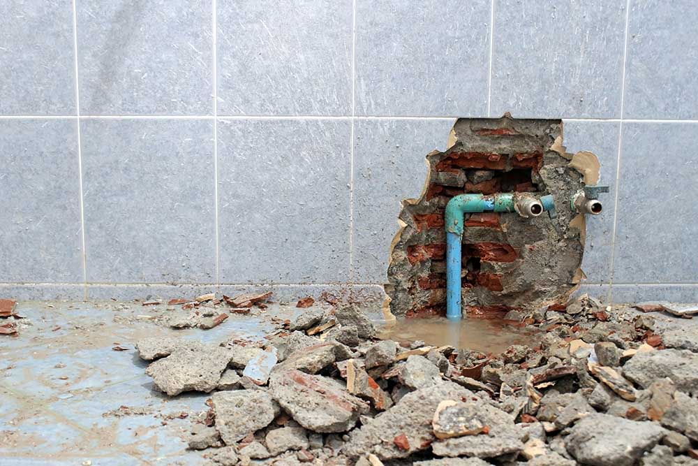 Water leak damaging a tiled wall and floor around an exposed pipe